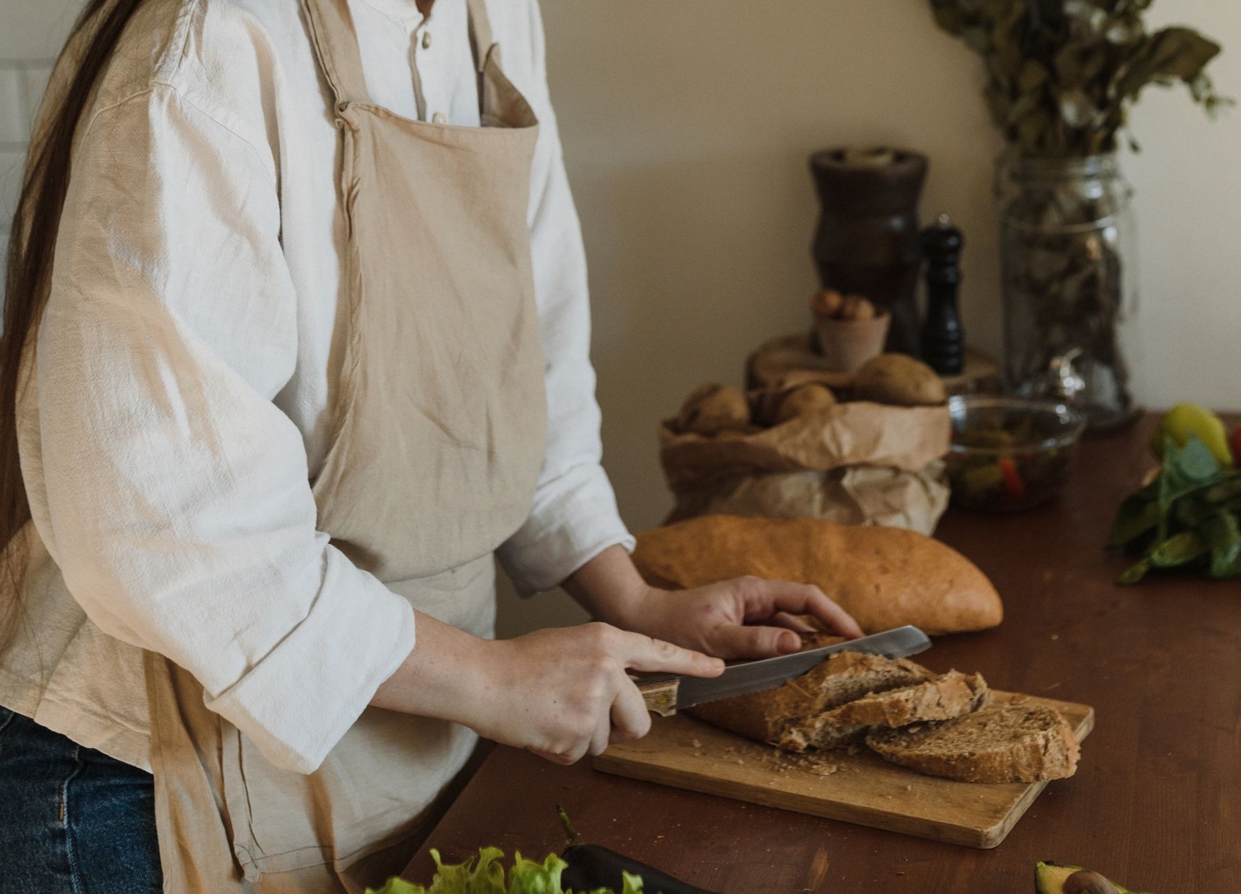 Hände schneiden frisches Brot auf einem Holzbrett in einer hellen Küche